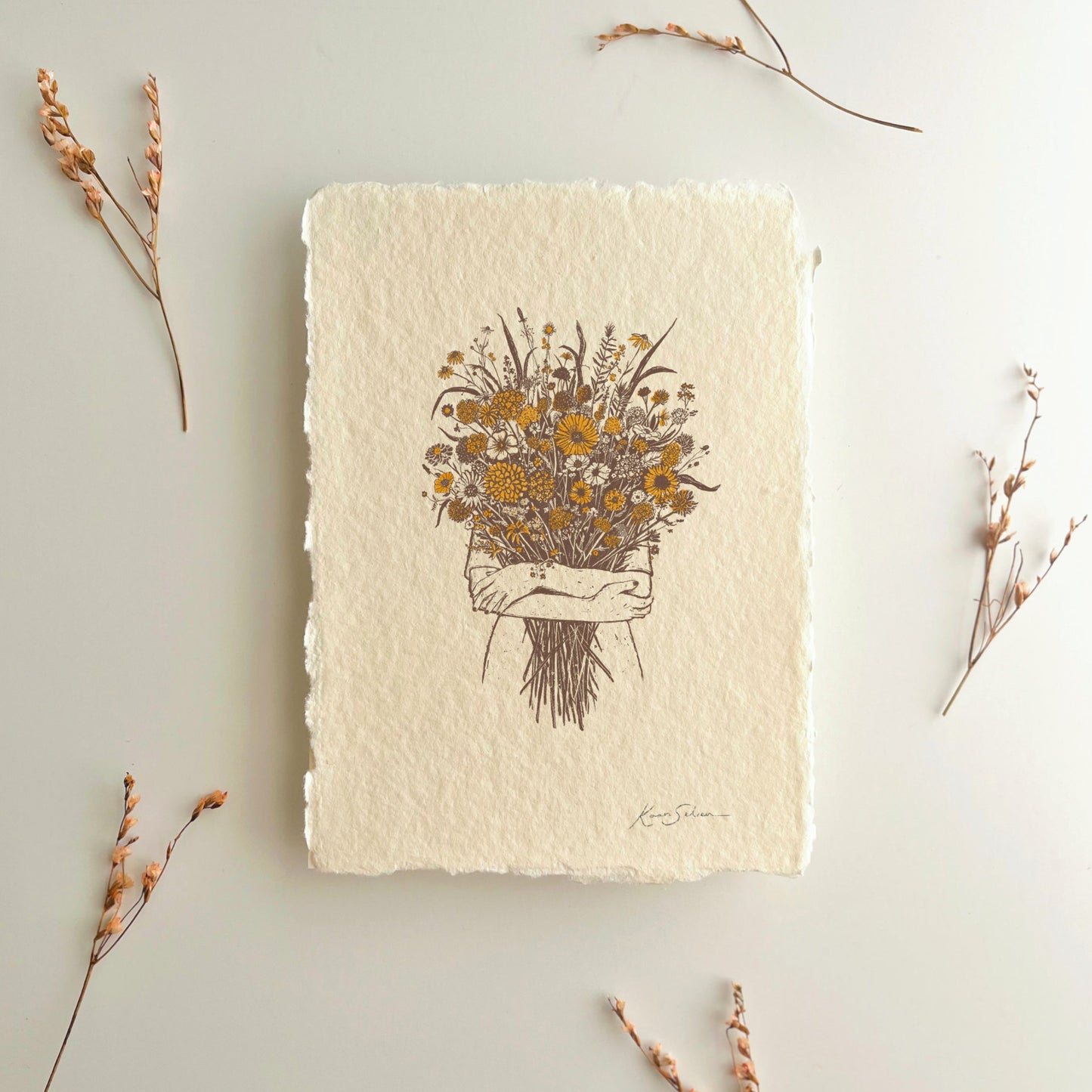Floral drawing printed on handmade paper with dried flowers laying around it on a light gray background